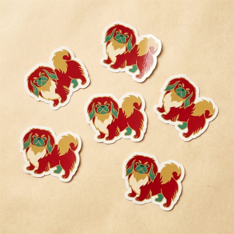 Small die-cut vinyl stickers of Pekingese dogs scattered on parchment paper